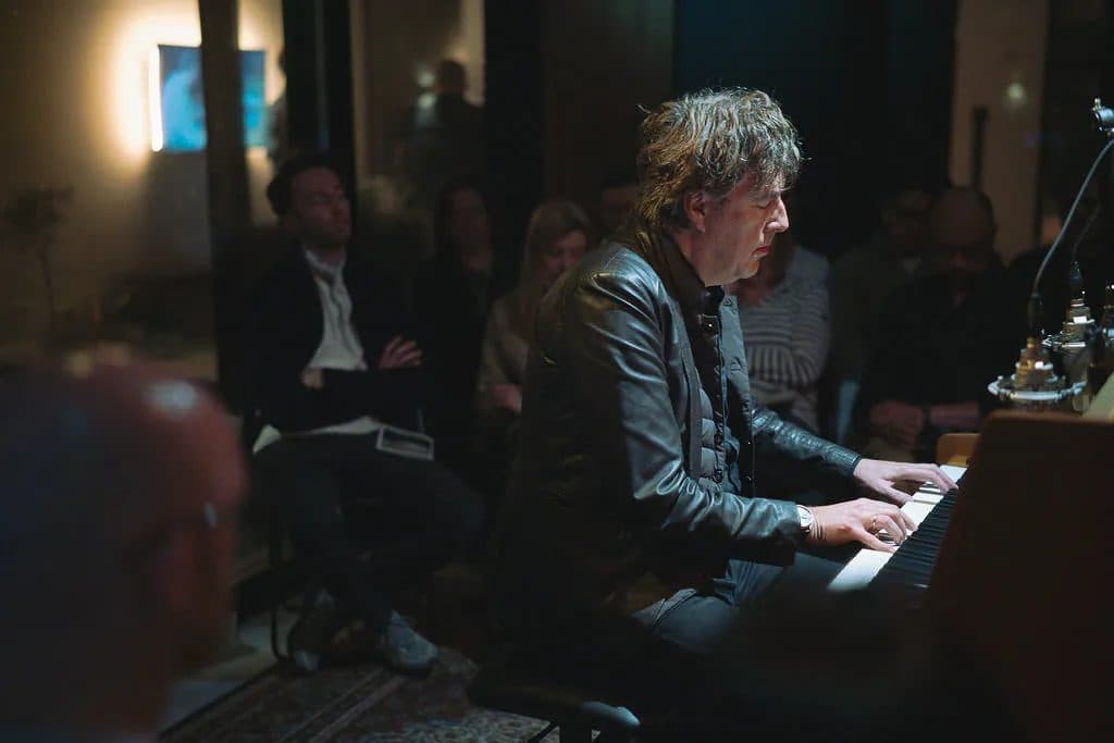 Pianist performing at the piano surrounded by a seated audience in warm light