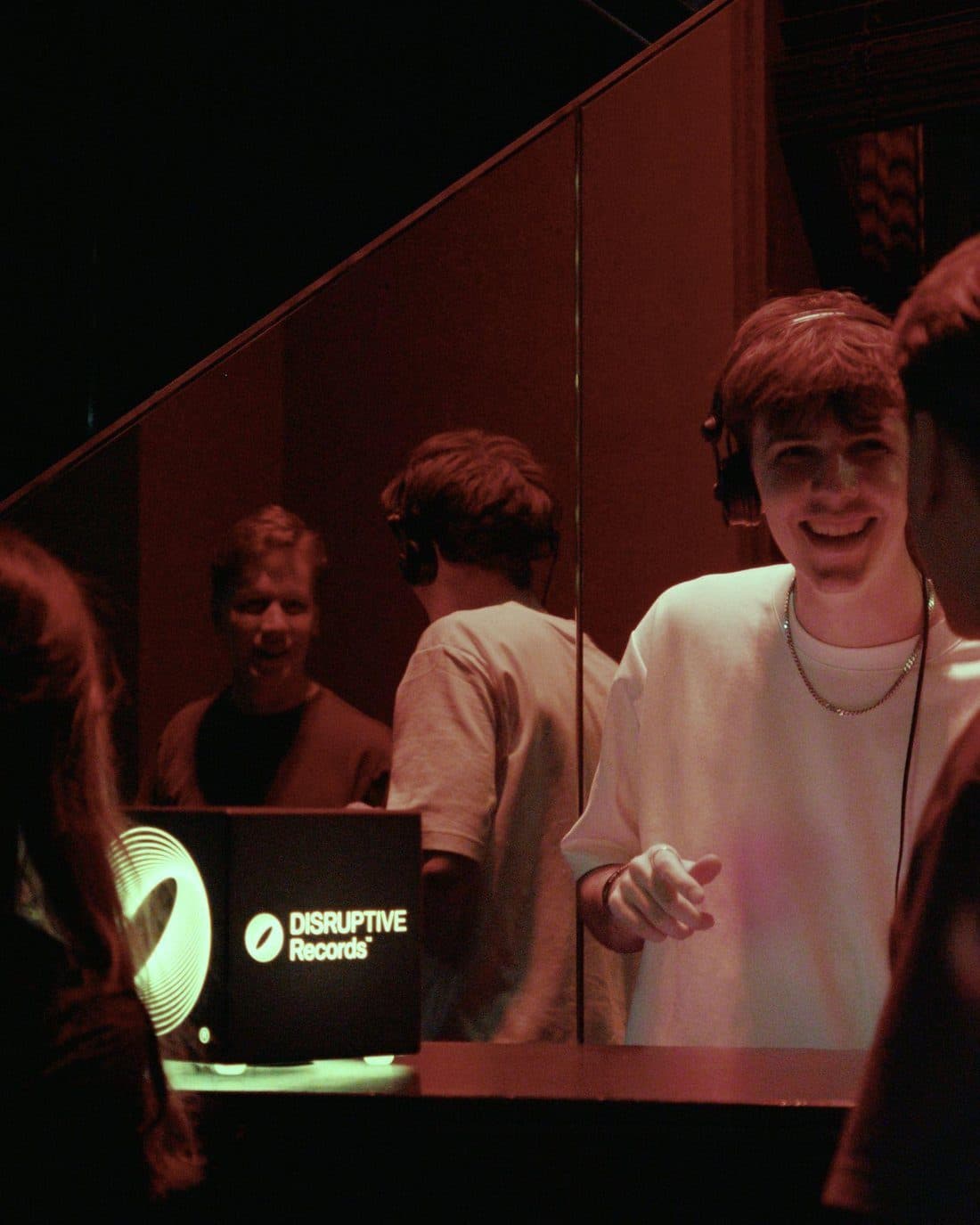 An artist with headphones at the Disruptive Records session desk, the label's spiral mark on the laptop lid, the room in red light
