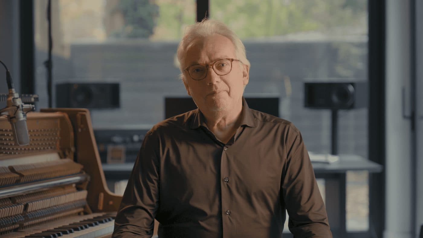 Ron Adelaar speaking on camera beside the opened piano in a MasterPiano masterclass film